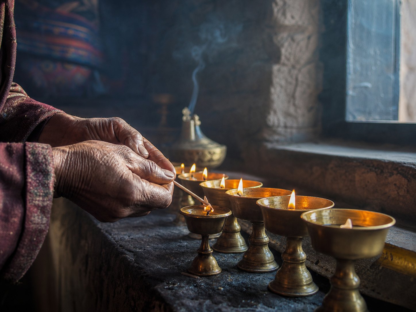 Hands lighting a row of butter lamps at dawn